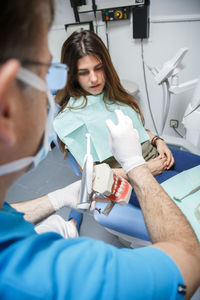 Professional doctor demonstration process of healthy teeth brushing to young woman sitting in chair.