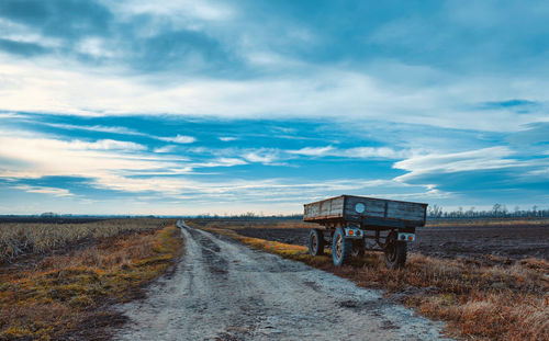 Dirt road amidst field against sky