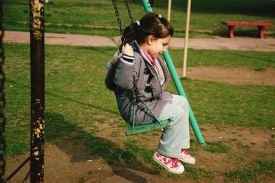 Side view of cute girl swinging in park