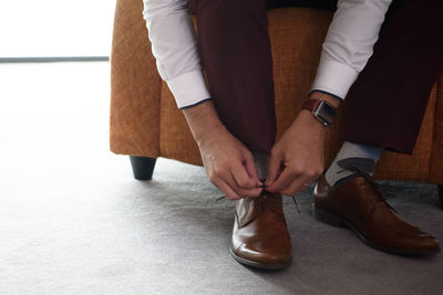 Low section of man tying shoe laces while sitting at home