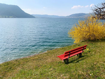 Empty bench by lake against sky