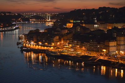 Illuminated buildings by river against sky at night