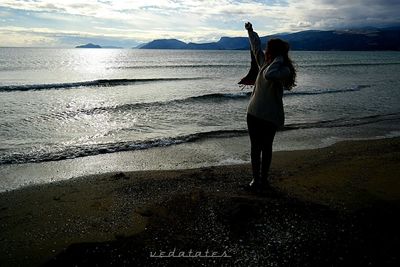 Woman photographing at beach against sky during sunset