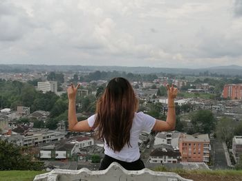 Rear view of woman gesturing peace sign while looking at cityscape