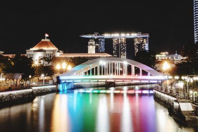 Illuminated bridge over river against buildings at night