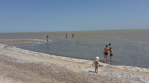 Children playing at beach against clear sky on sunny day