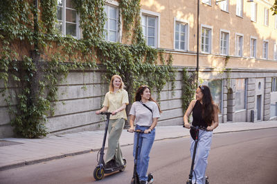 Young female friends spending time together outdoors riding electric scooters
