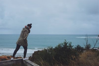 Full length of woman standing on retaining wall against beach