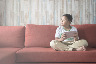 Boy holding digital tablet while sitting on sofa at home