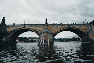 Arch bridge over river against sky during rainy season