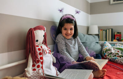 Portrait of smiling girl wearing fairy costume while sitting with book on bed at home