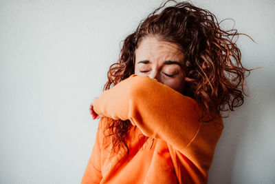 Woman covering face with hand against wall