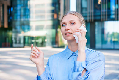 Successful female banker using smart phone outdoors while standing near office