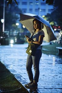 Young woman with umbrella standing on footpath during rainy season