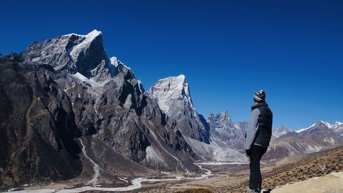 Man standing on rock against blue sky