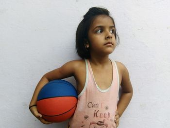Girl holding ball while standing against wall