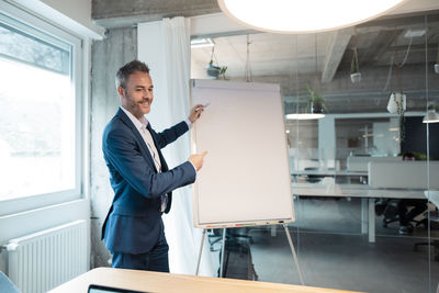 Smiling businessman writing on flipchart gesturing at office