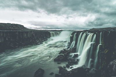 View of waterfall against cloudy sky