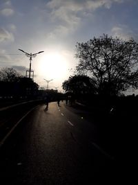 Street amidst silhouette trees against sky at sunset