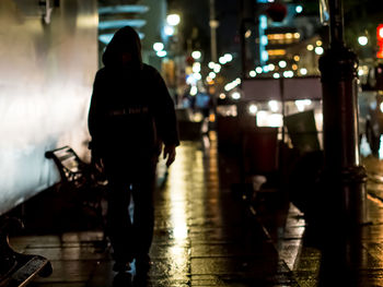 Rear view of man walking on illuminated street at night