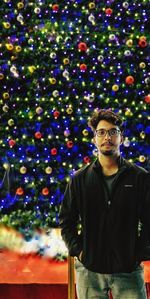 Portrait of young man standing against illuminated christmas tree