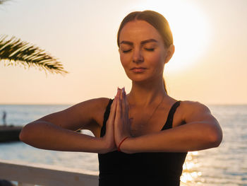 Close-up of young woman meditating on beach against clear sky