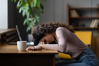 Overworked tired female freelancer or remote worker sleep on desk with laptop suffer from fatigue