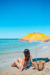 Rear view of woman sitting at beach against clear blue sky