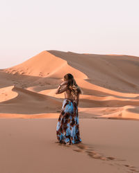 Woman standing on sand dune in desert against sky