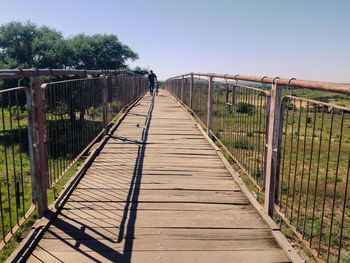 Rear view of man walking on footbridge against clear sky