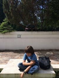 High angle view of sad boy sitting with backpack on retaining wall