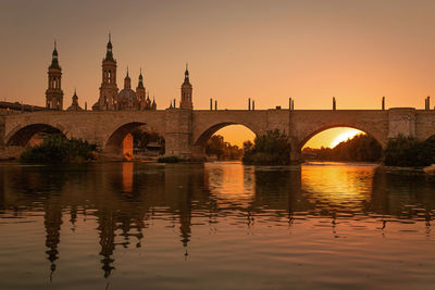 Arch bridge over river against buildings during sunset