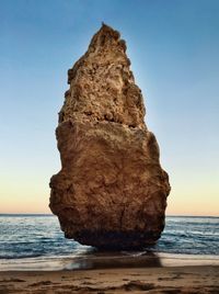 Rock formation on beach against sky during sunset