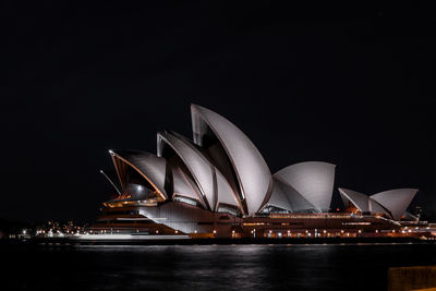 Illuminated ferris wheel in city against clear sky at night