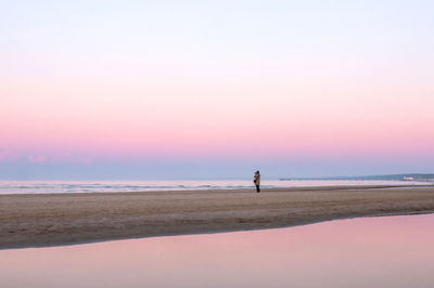 Rear view of woman walking at beach against clear sky