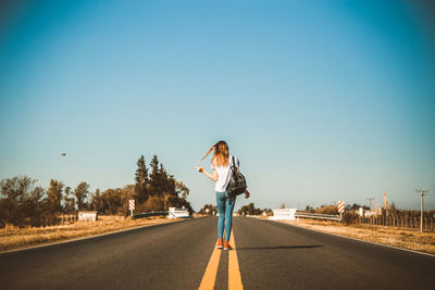 Rear view of woman standing on road against clear blue sky