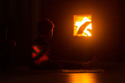 Silhouette boy against illuminated by fire at home