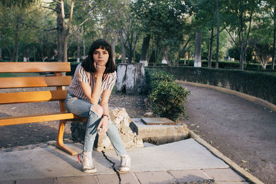 Portrait of young woman sitting on bench against trees