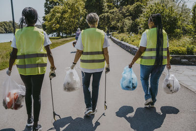 Rear view of female environmentalists with plastic bags walking on street