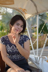 Portrait of smiling young woman with finger on lips sitting on bench