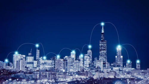 Illuminated cityscape with connecting dots against clear blue sky at night