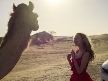 Kind girl in red dress met camel in dubai desert