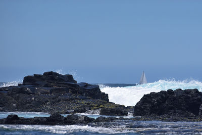 Rock formations by sea against clear blue sky