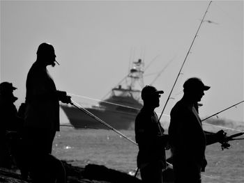 Silhouette of people working by sea against sky