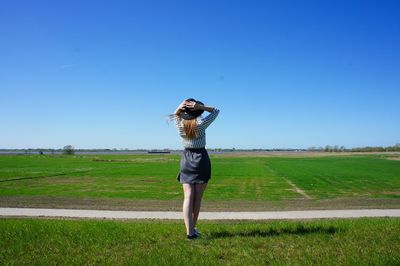 Rear view of woman wearing hat standing on grassy field against sky during sunny day
