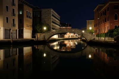 Illuminated bridge over river by buildings in city at night
