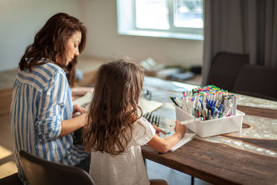 Rear view of mother and daughter drawing at home