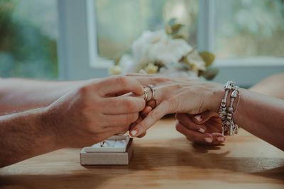 Cropped hand of man putting ring in woman finger on table