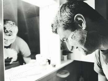 Close-up of man with shaving cream standing in bathroom at home 