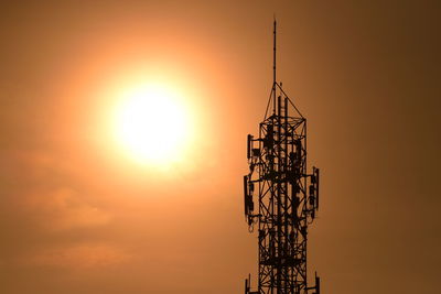 Silhouette of communications tower against orange sky